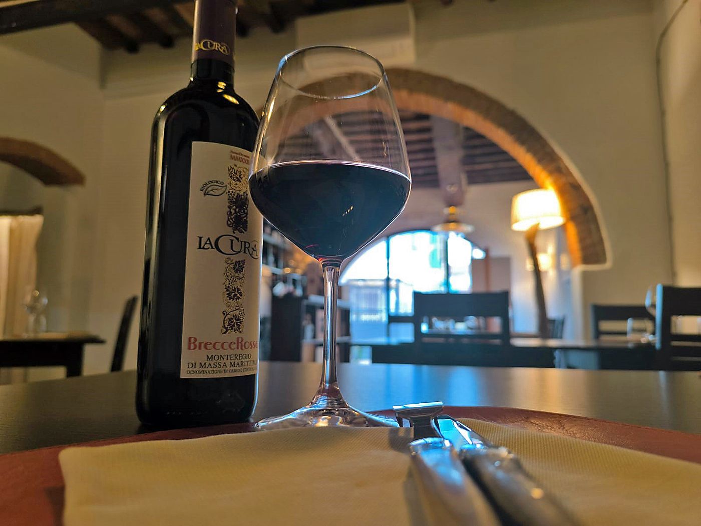 Calice di vino rosso versato, atmosfera calda — enoteca Follonica